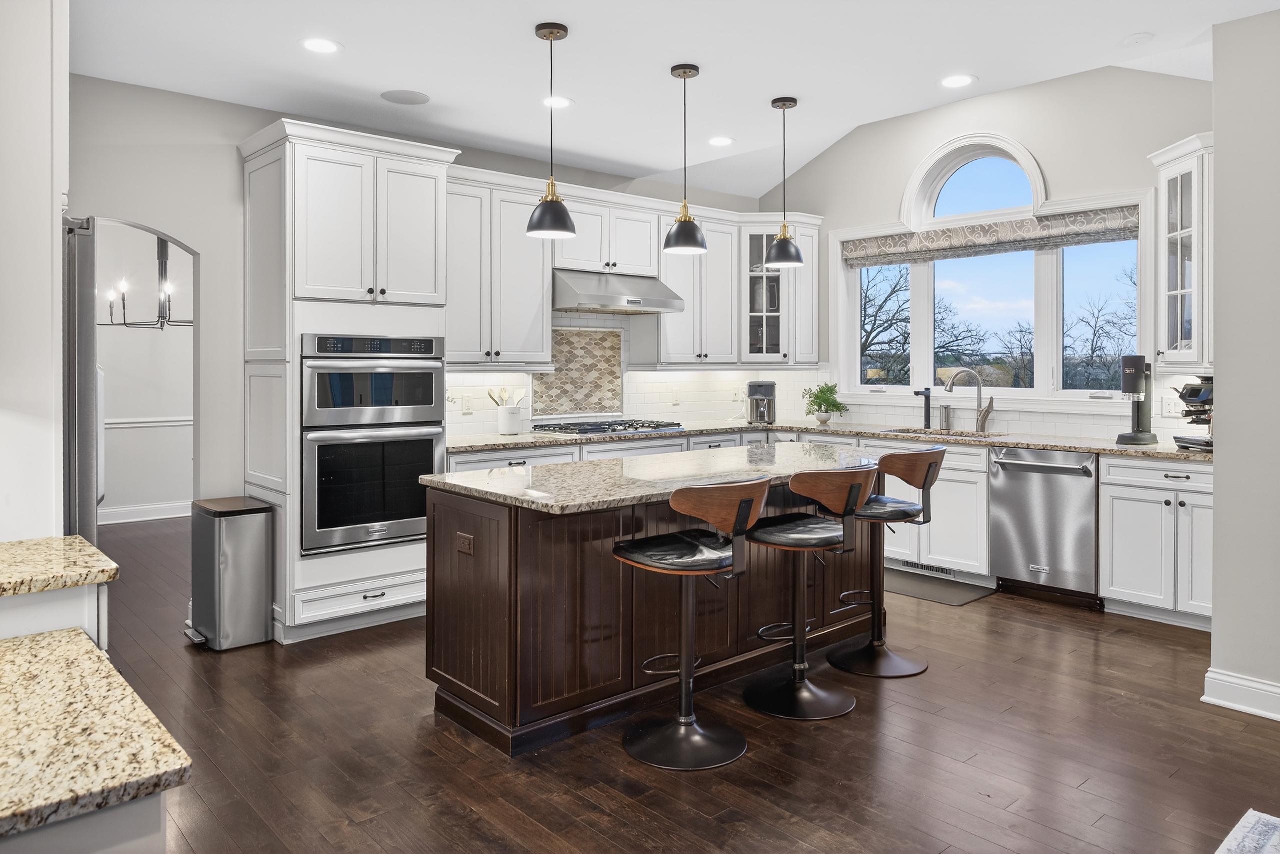 Chef's kitchen with white cabinetry, granite center island, pendant lights, and stainless steel dual ovens